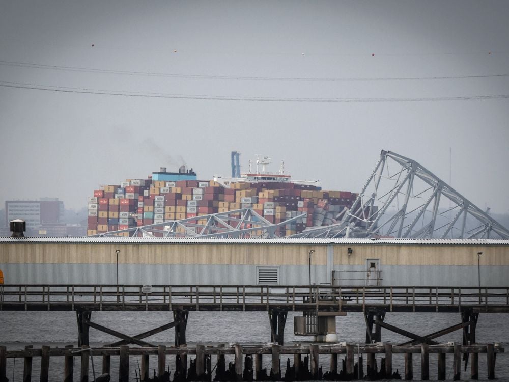 a large container ship in a river with ruins of a truss bridge on top of it